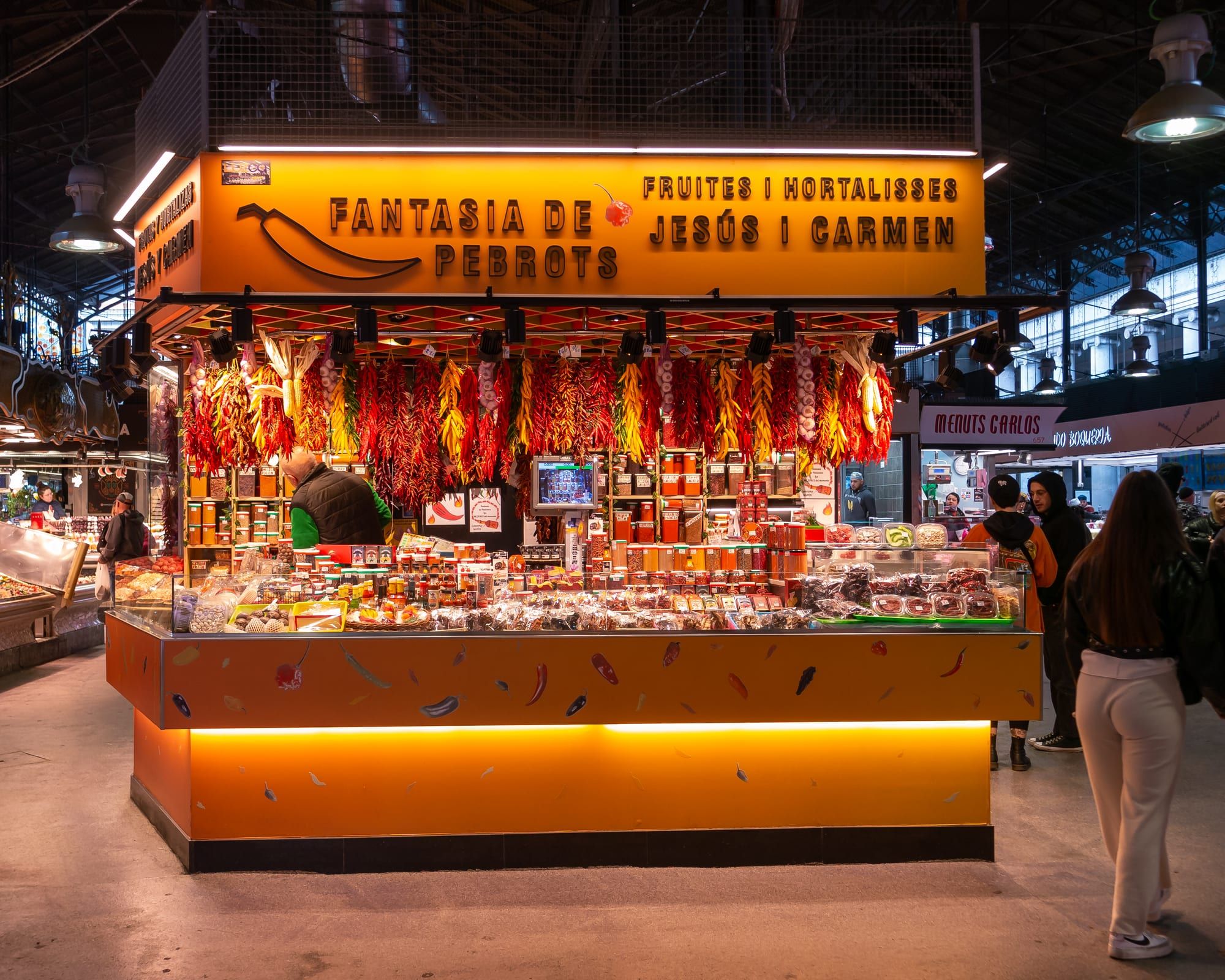 A brightly lit fruit-and-vegetable stall hung with strings of dried red peppers inside the Mercat de la Boqueria