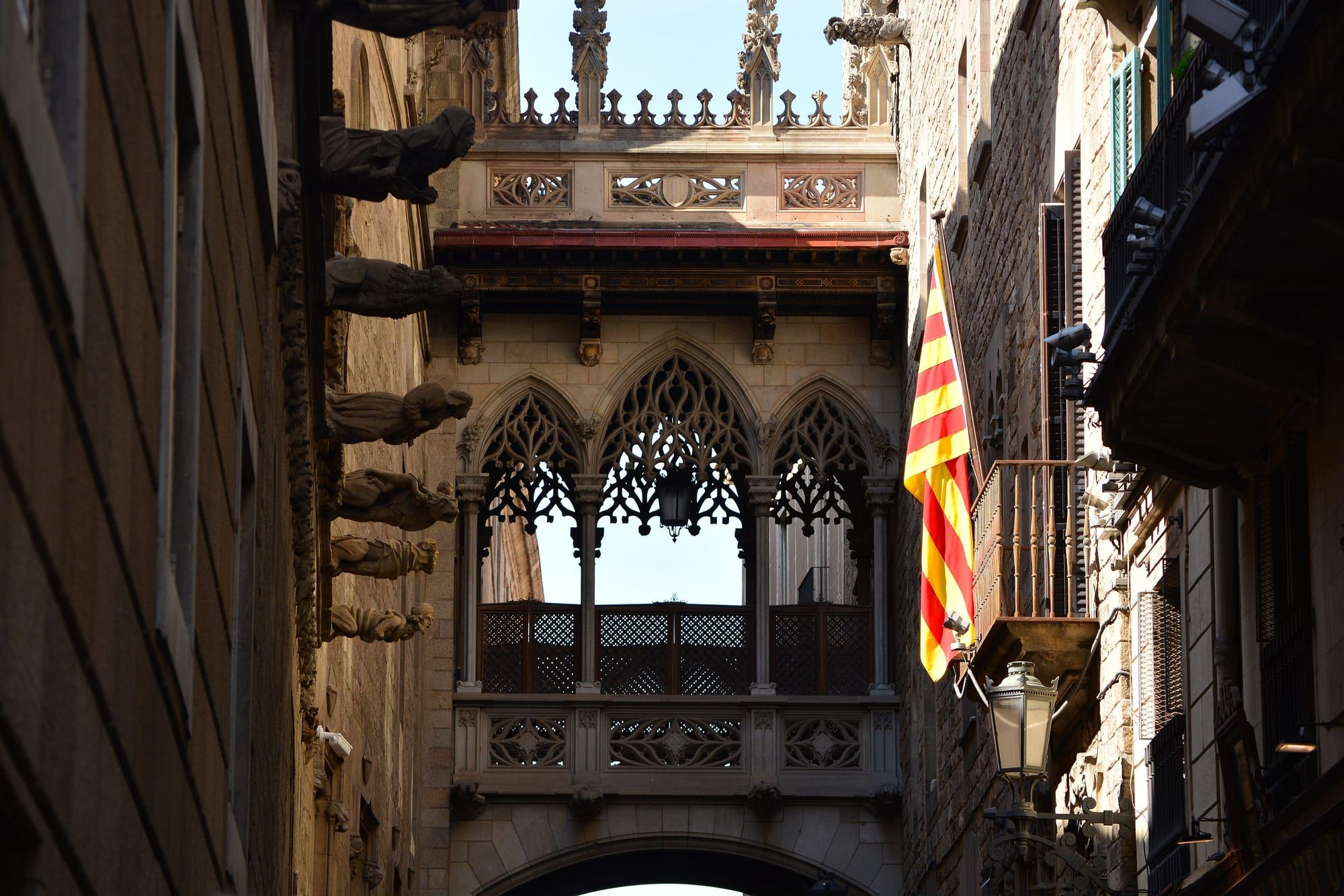 The neo-Gothic stone bridge over Carrer del Bisbe in the Gothic Quarter, with gargoyles and a Catalan flag on a balcony