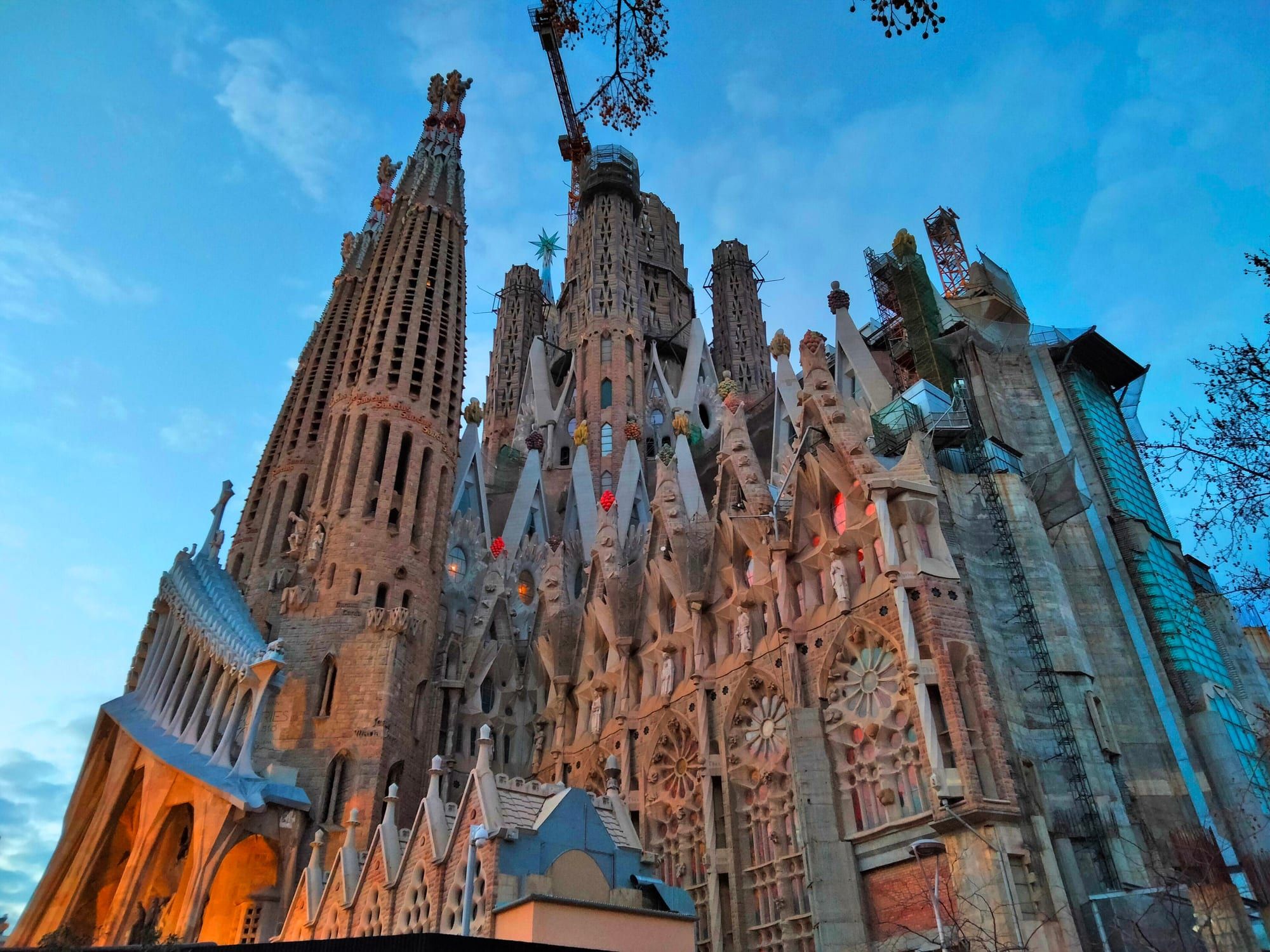 The stone spires of the Sagrada Família basilica seen from below, from the corner of Carrer de Sardenya and Carrer de Mallorca, against a blue sky