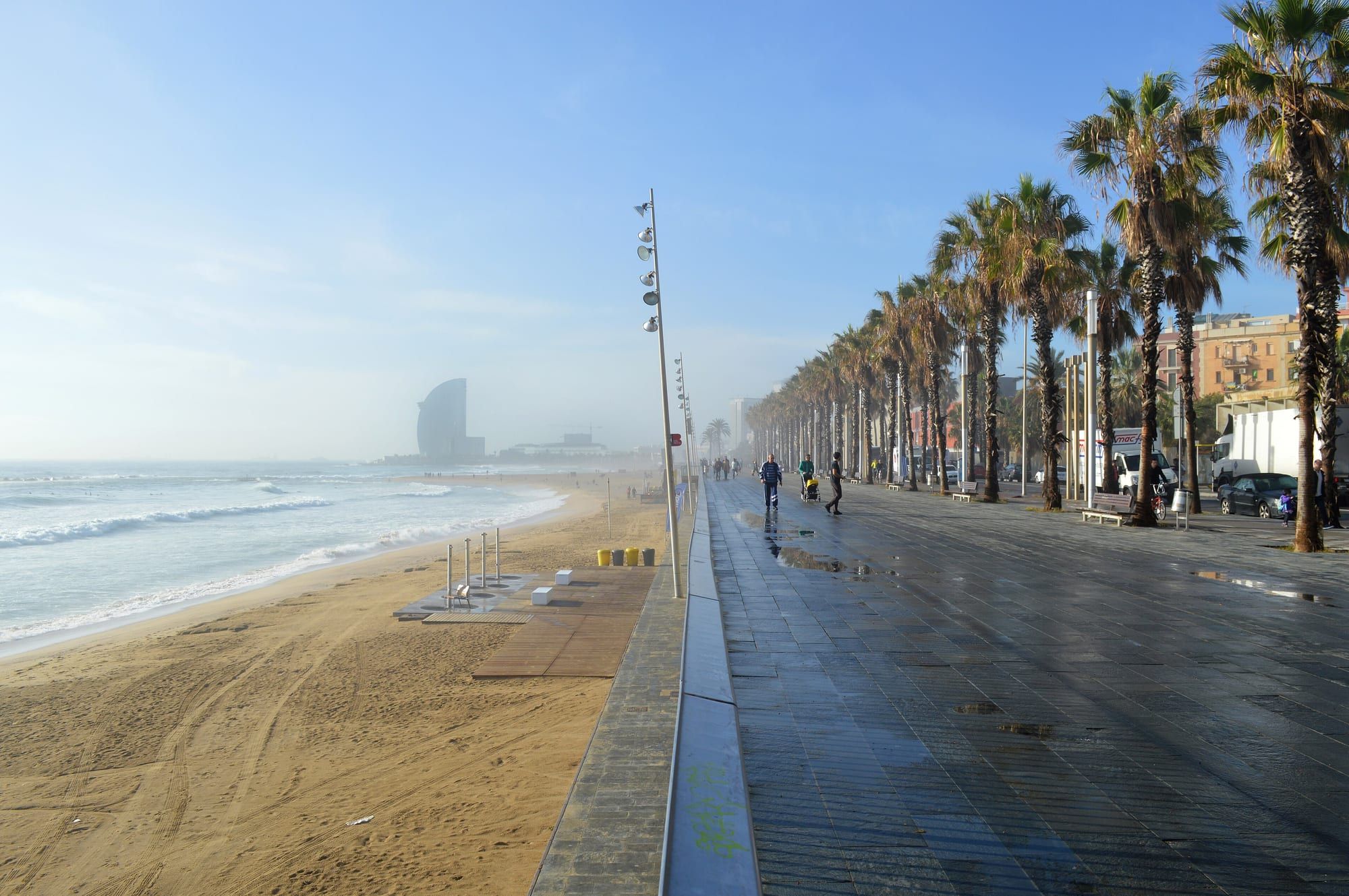 The palm-lined promenade and sandy Barceloneta beach on a quiet morning, with the W Hotel in the distance